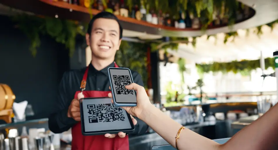 Customer scanning TableQR restaurant QR code menu held by a smiling server inside a modern cafe.