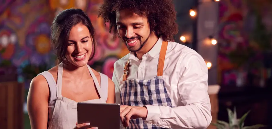 Two restaurant staff smiling as they manage their digital menu on a tablet in a cozy cafe.