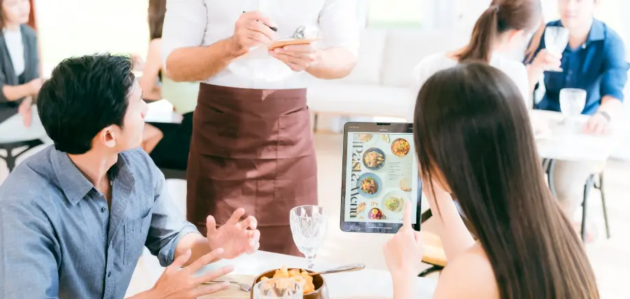 Waiter taking an order from a couple while they browsing TableQR digital restaurant menu on a tablet at the table.