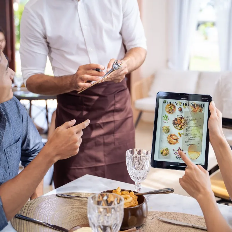 Waiter taking an order at the table while guests read the tablet menu